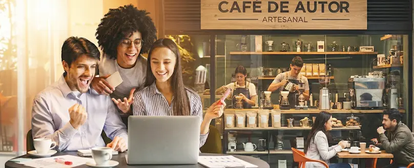 Grupo de jóvenes emprendedores trabajando felices en su laptop desde una cafetería, impulsando su posicionamiento con el Plan StartUP de nuestra agencia de marketing digital en Quito.